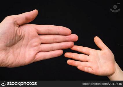 Closeup of small and big caucasian hand palms touching isolated towards black background