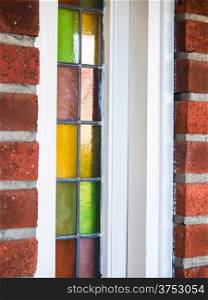 Closeup of small colored glass windows with white frame in a red brick building