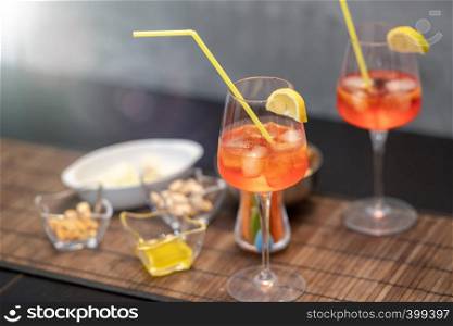Closeup of some glasses with cocktails with straws and nuts on a brown table.