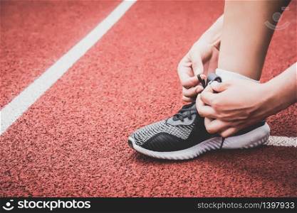 Closeup of sport woman tying sneakers shoelace rope at running track lane in stadium. Sport center and Fitness gym concept. Healthy and Body build up theme. Sportswear and Fashion theme