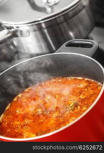 Closeup of tasty red boiling ukrainian borsch in pan on the cooker, homemade delicious food, healthy tomato soup