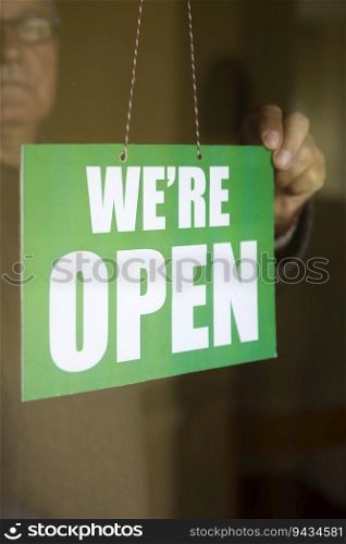 Closeup of the business owner hanging an open sign at a glass door