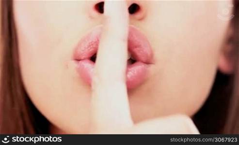 Closeup of the lips of a sensual woman giving a shushing gesture raising her finger to her lips as she asks for silence