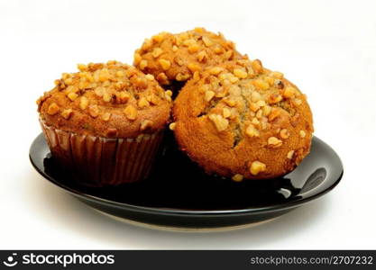 Closeup of three banana nut muffins topped with crushed walnuts on a black saucer with a light colored background.. Banana Muffin