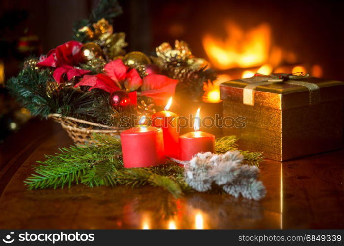 Closeup of three burning Christmas candles on table next to gift box and decorative wreath