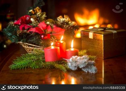 Closeup of three burning Christmas candles on table next to gift box and decorative wreath