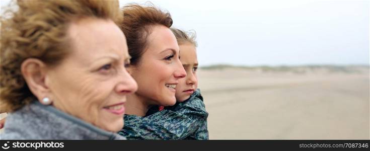 Closeup of three generations female looking at sea on the beach in autumn. Background focus on young woman and child. Three generations female looking at sea