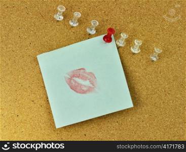 closeup of thumbtacks and kiss note on cork board