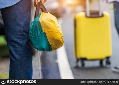 Closeup of tourist legs walking along road with bag during travel in countryside. People lifestyles and vacation concept. Man holding and backpacking for long holiday trip with mountain background