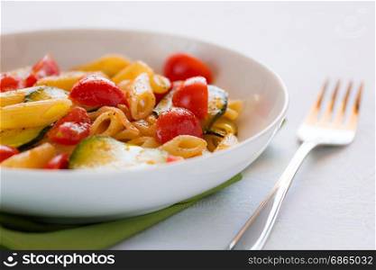 Closeup of traditional italian penne pasta with zucchini and cherry tomatoes seasoned with oil and black pepper. Italian penne pasta with zucchini and cherry tomatoes
