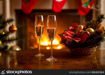 Closeup of two glasses of champagne in front of burning fireplace