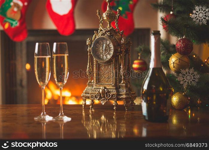 Closeup of two glasses of champagne on table next to old clock showing midnight at living room decorated for Christmas