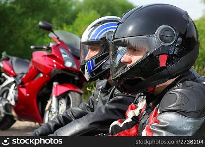 closeup of two motorcyclists sitting on country road near bikes