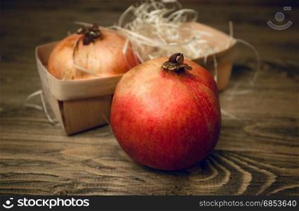 Closeup of two pomegranates lying in basket on old wooden desk