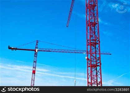 Closeup of two red tower construction cranes against blue sky