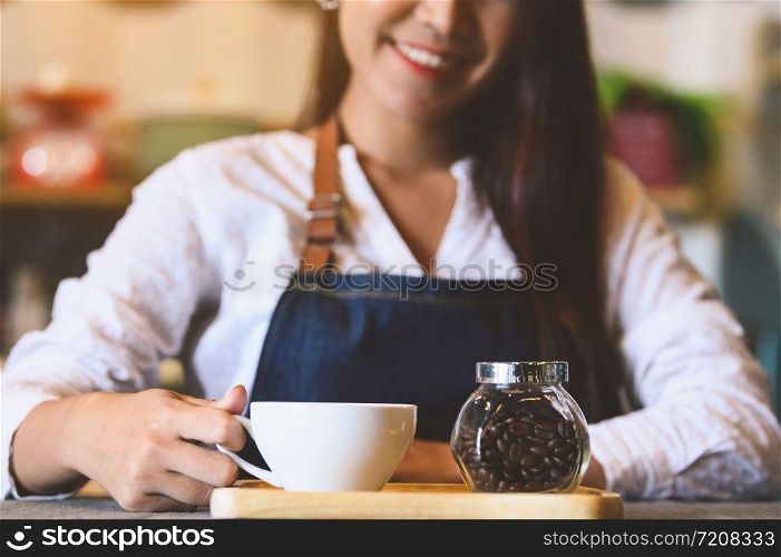 Closeup of white coffee cup with beautiful Asian woman barista background for serving to customer. Job and occupation. Food and drink beverage. Coffee shop and Cafe. Business and restaurant ownership