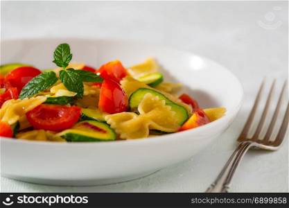 Closeup of whole farfalle pasta with zucchini, cherry tomatoes and red onion. Whole farfalle pasta with zucchini, cherry tomatoes and red onion