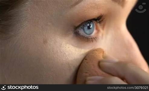 Closeup of woman&acute;s face applying concealer under eye with beauty blender sponge - video in slow motion