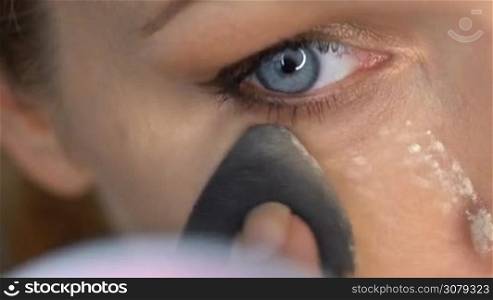 Closeup of woman&acute;s face applying loose powder under eye with beauty blender sponge - video in slow motion