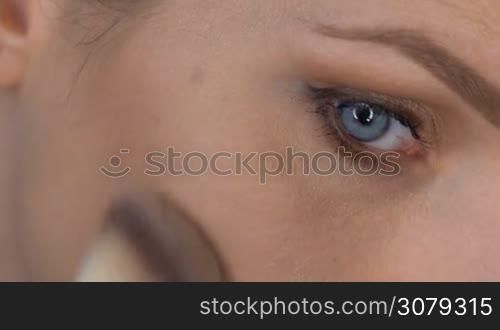 Closeup of woman&acute;s face applying makeup with brush to cheekbone - video in slow motion