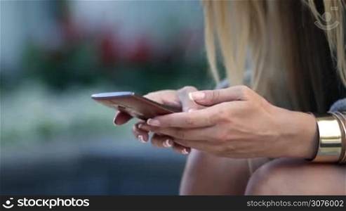 Closeup of woman&acute;s hands browsing a cellphone in the park sitting on the bench