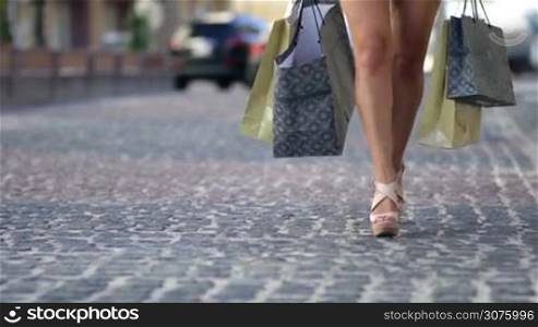 Closeup of woman&acute;s legs with shopping bags walking along the city street after day shopping