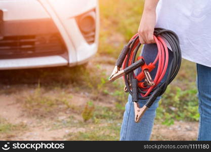 Closeup of woman hand holding battery cable copper wire for repairing broken car by connect battery with red and black line to electric terminal by herself. Car maintenance and transportation concept