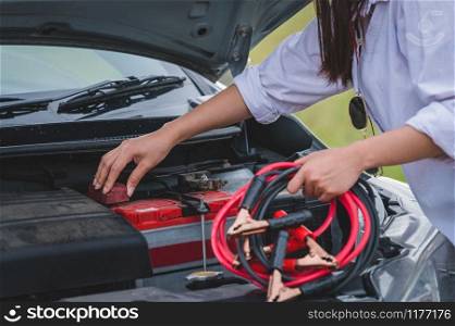 Closeup of woman hand holding battery cable copper wire for repairing broken car by connect battery with red and black line to electric terminal by herself. Car maintenance and transportation concept