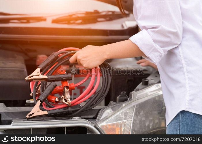Closeup of woman hand holding battery cable copper wire for repairing broken car by connect battery with red and black line to electric terminal by herself. Car maintenance and transportation concept