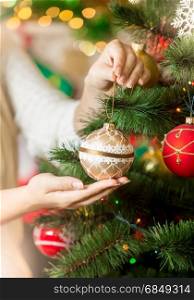 Closeup of woman in sweater decorating Christmas tree with baubles