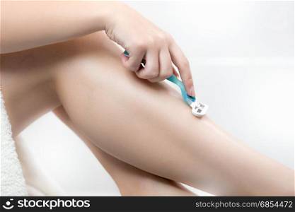 Closeup of woman removing hair on legs with razor