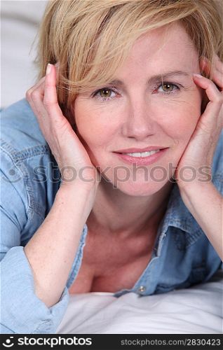 Closeup of woman resting her head in her hands while lying on bed