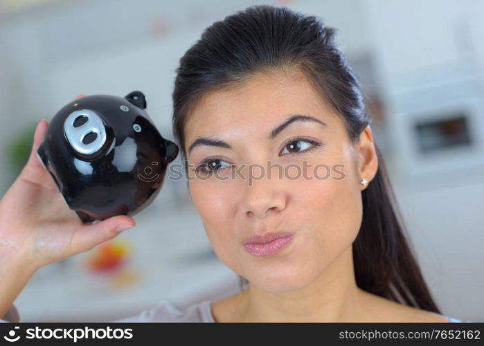 closeup of woman shaking piggybank dubious expression