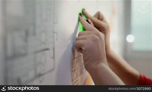 Closeup of woman sticking adhesive note to a blueprint, writing tasks to complete the housing project. Closeup, copy space