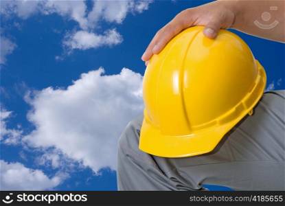 Closeup of yellow helmet at builder hands on blue sky background