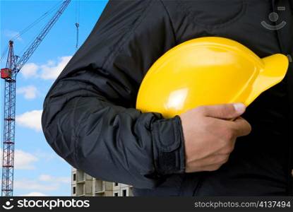 Closeup of yellow helmet at builder hands on building background