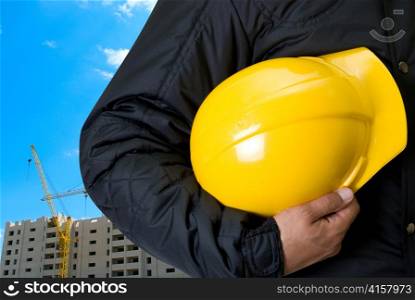 Closeup of Yellow helmet at builder hands on building background