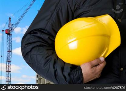 Closeup of Yellow helmet at builder hands on building background