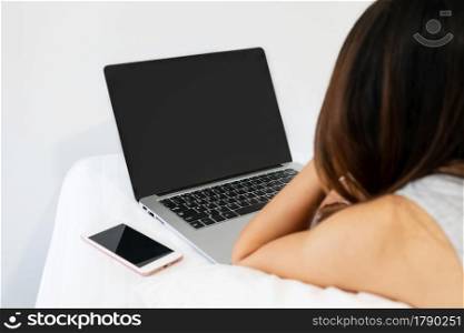 Closeup of young Asian woman using computer on bed in the morning. Technology and lifestyle, work from home concept. Copy space