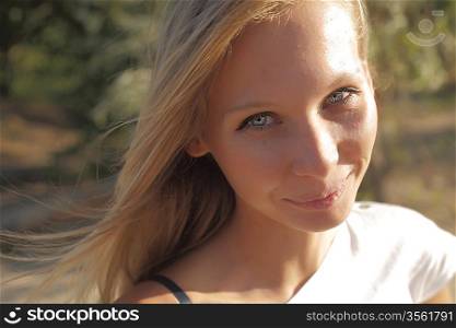Closeup of young beautiful smiling blond woman, on green background of summer nature