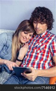 Closeup of young happy couple in love embraces looking electronic tablet while resting over a bed. Leisure time at home concept.. Happy couple in love looking electronic tablet on bed