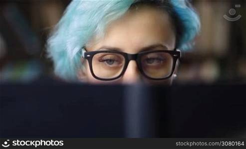 Closeup of young hipster woman in trendy eyeglases reading a book. Portrait of nerdy student girl behind book cover with only eyes visible. Face expression, emotions, attitude, reaction and education concept.
