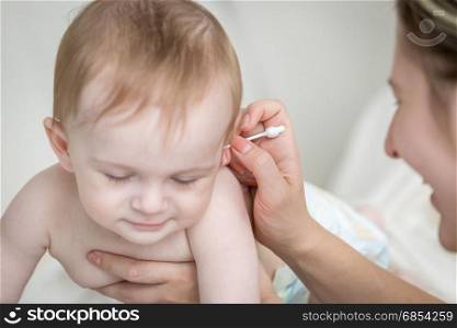 Closeup of young mother cleaning baby&rsquo;s ear with cotton swab