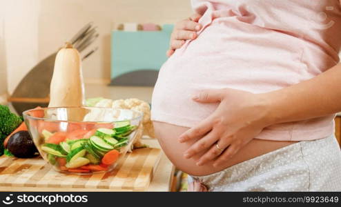 CLoseup of young pregnant woman cooking and eating vegetable salad holding big abdomen and touching it with hands.. CLoseup of young pregnant woman cooking and eating vegetable salad holding big abdomen and touching it with hands