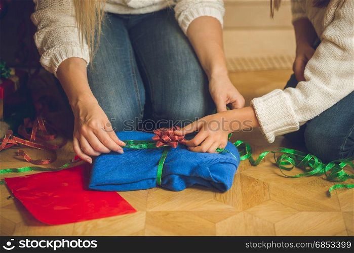 Closeup of young woman and girl wrapping sweater in decorative paper and colorful ribbons