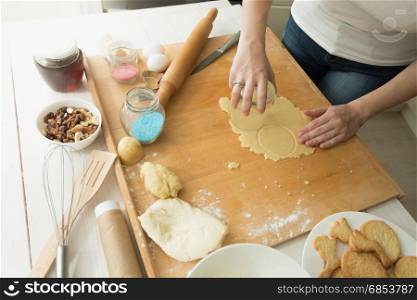 Closeup of young woman cutting dough with glass