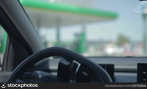 Closeup of young woman driving car in the city and coming to gas station. View from back seats of car