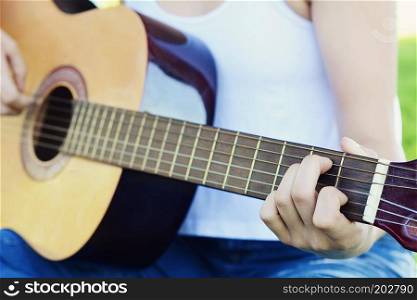 Closeup of young woman hands playing acoustic guitar at the park.