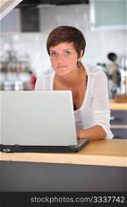 Closeup of young woman in kitchen with laptop computer