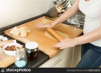 Closeup of young woman rolling dough on wooden board with pin